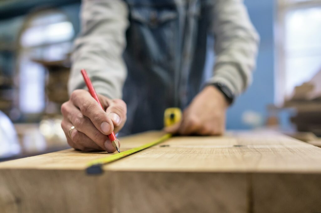 Carpenter measuring and tracing line with a ruler and pencil on wooden timber.